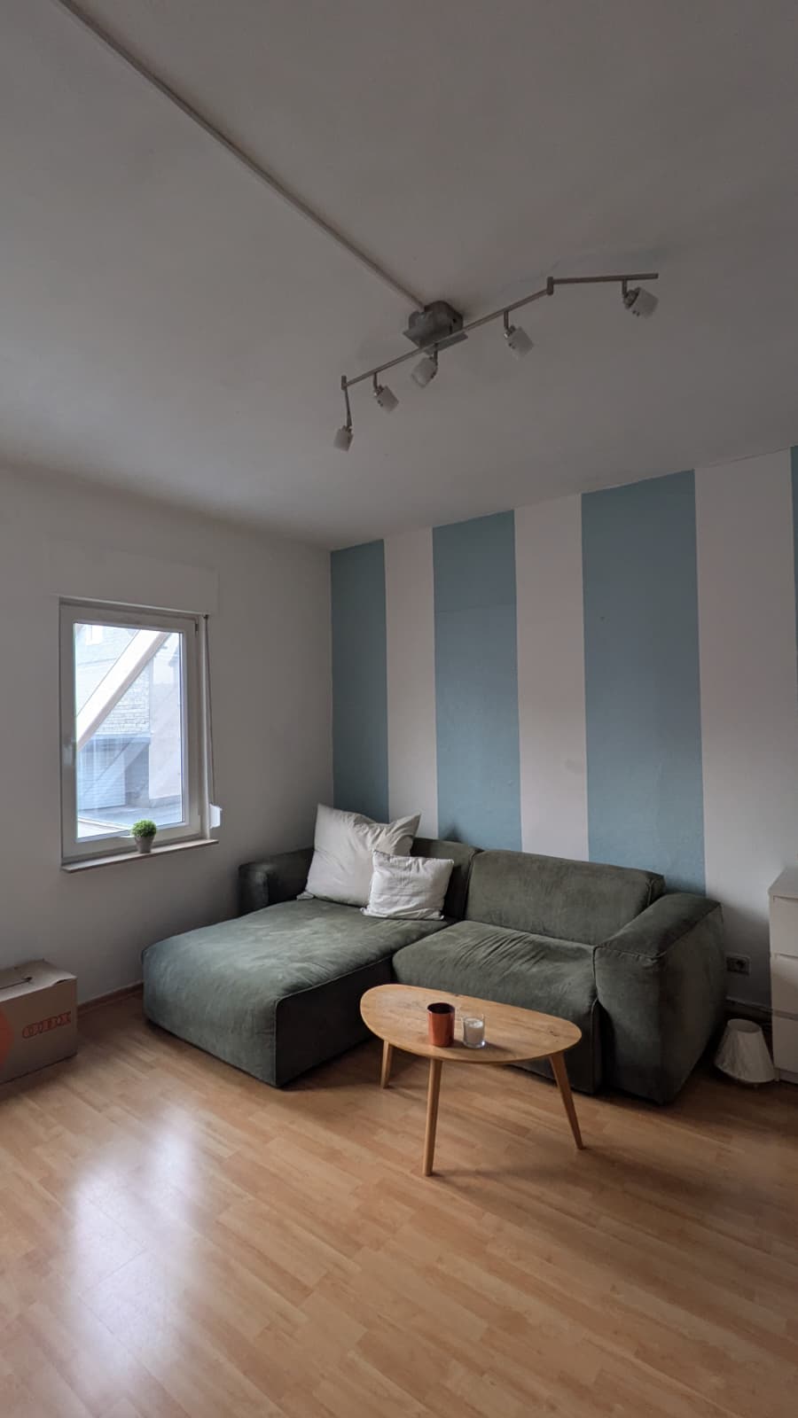 Wohnzimmer mit grünem Sofa, Holztisch und blau-weiß gestreifter Wand